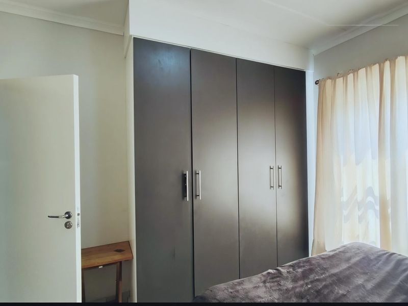 A bedroom featuring dark built-in cupboards with modern handles and neutral wall finishes.