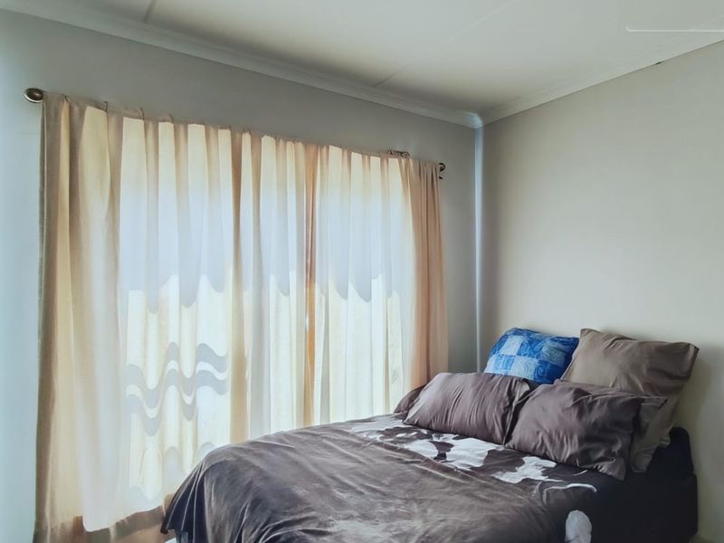 A bedroom featuring neutral wall finishes and a large window dressed with curtains.