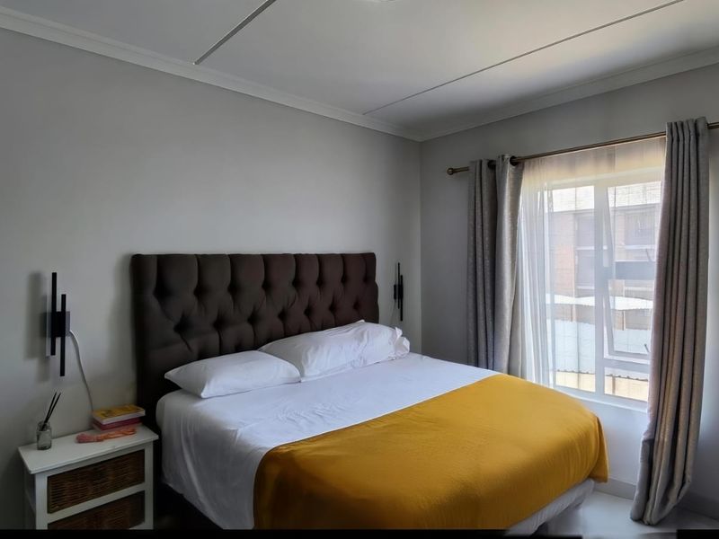 A well-lit bedroom featuring neutral walls, a window with curtain treatments, and coving detail.