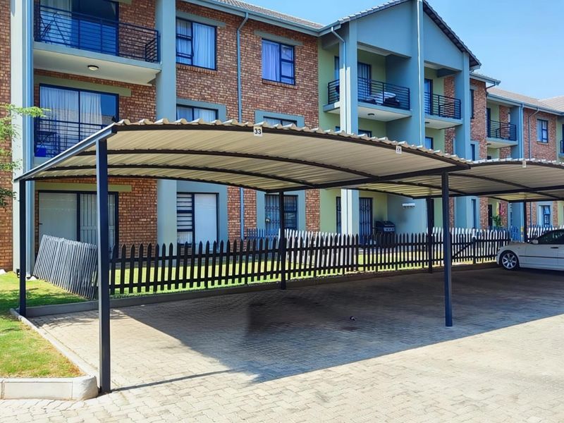 Exterior view of the apartment complex featuring a covered carport area with paved driveway and multi-story brick and painted facade.