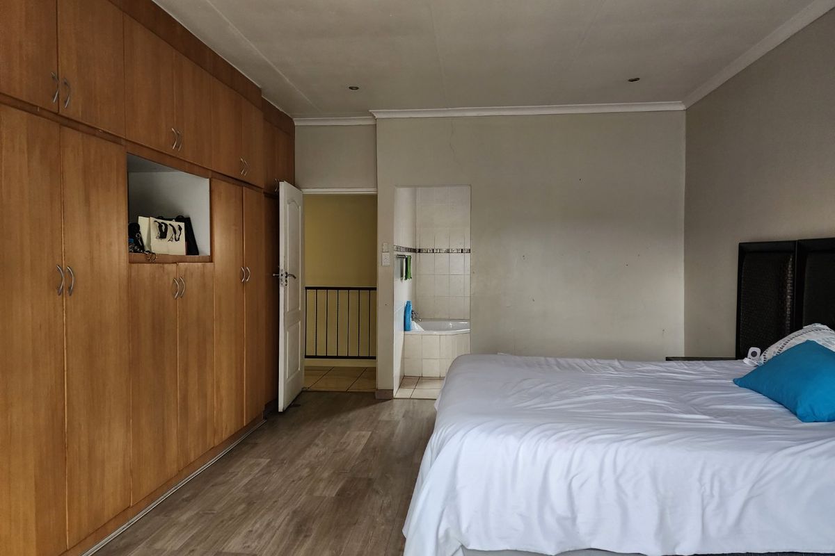 Spacious bedroom featuring extensive built-in wooden cupboards, laminate flooring, recessed lighting, and direct access to an en-suite bathroom.