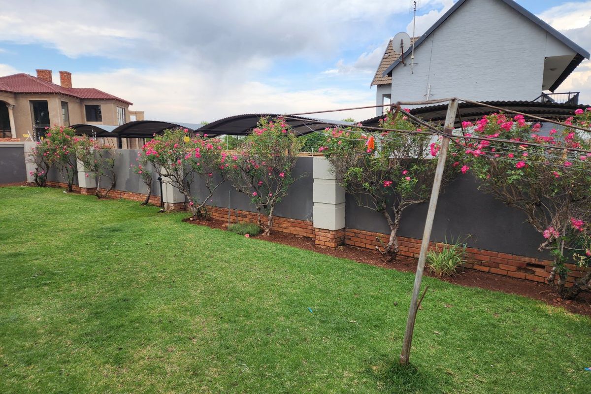A well-maintained rear garden featuring a solid boundary wall with brick detailing, concrete pillars, and an adjacent carport structure.