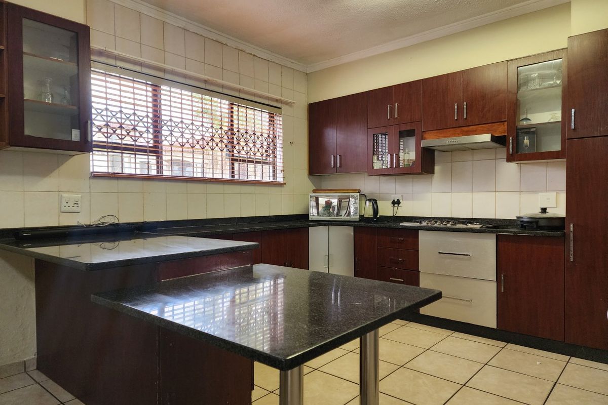 A functional kitchen featuring dark wood cabinetry, granite countertops, a gas hob with extractor fan, and tiled flooring with a window security gate.