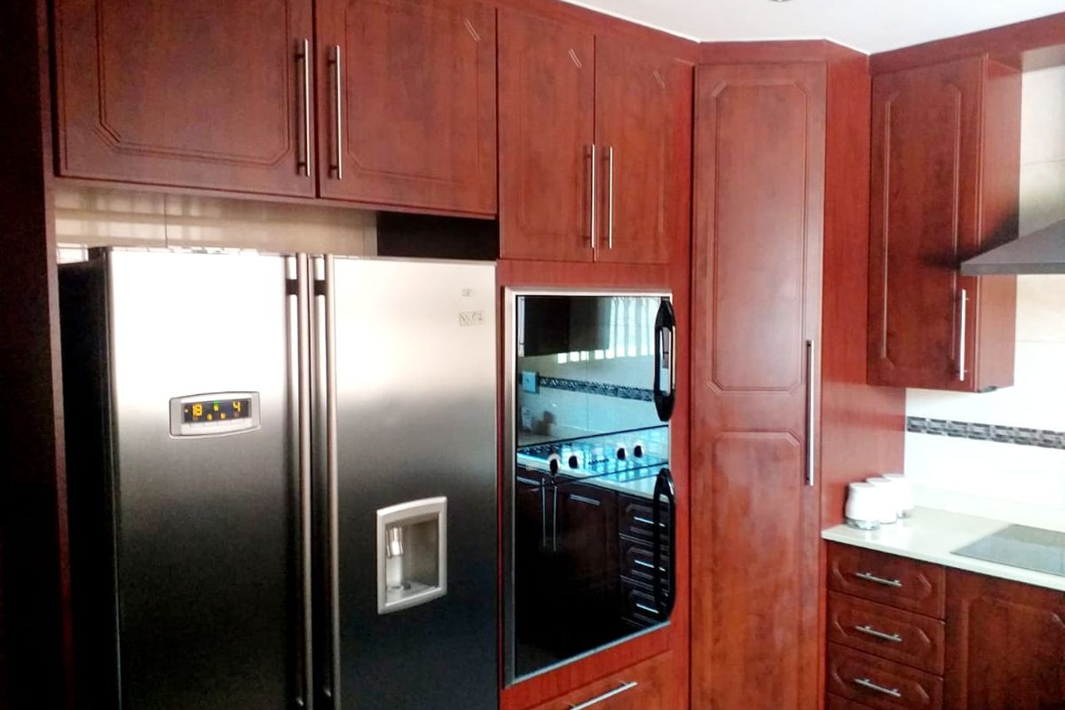 A kitchen featuring dark wood cabinetry, built-in oven, extractor fan, and a tiled backsplash, providing a functional and classic cooking space.