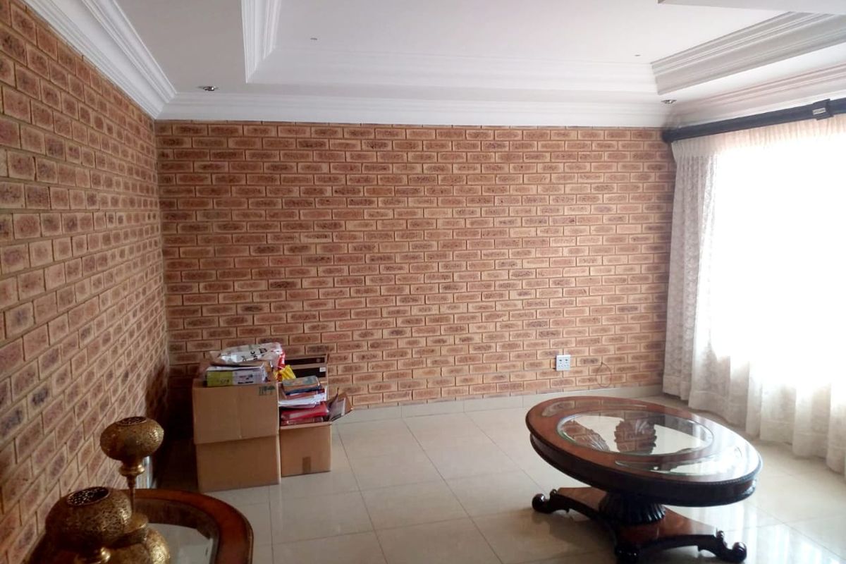 A living room featuring exposed brick walls, a decorative tray ceiling with recessed lighting, and neutral tiled flooring.