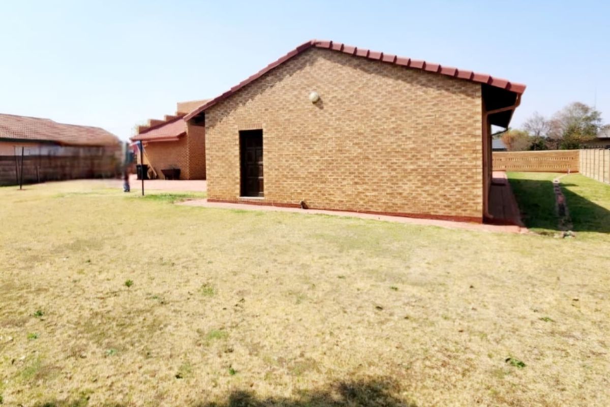 A view of the rear exterior of the house featuring face brick walls, a tiled roof, and a spacious backyard area.