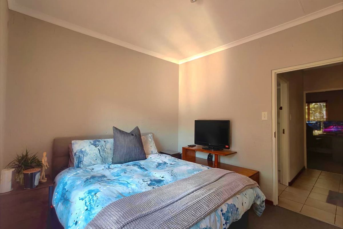 A standard bedroom featuring neutral wall tones, tiled flooring, and a doorway leading to an adjacent hallway.