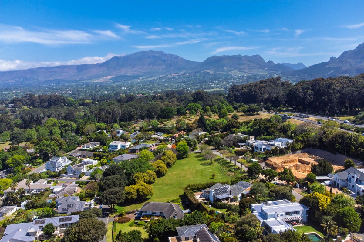 An elevated aerial view showcasing the surrounding residential neighborhood, lush green landscapes, and scenic mountain vistas in the distance.