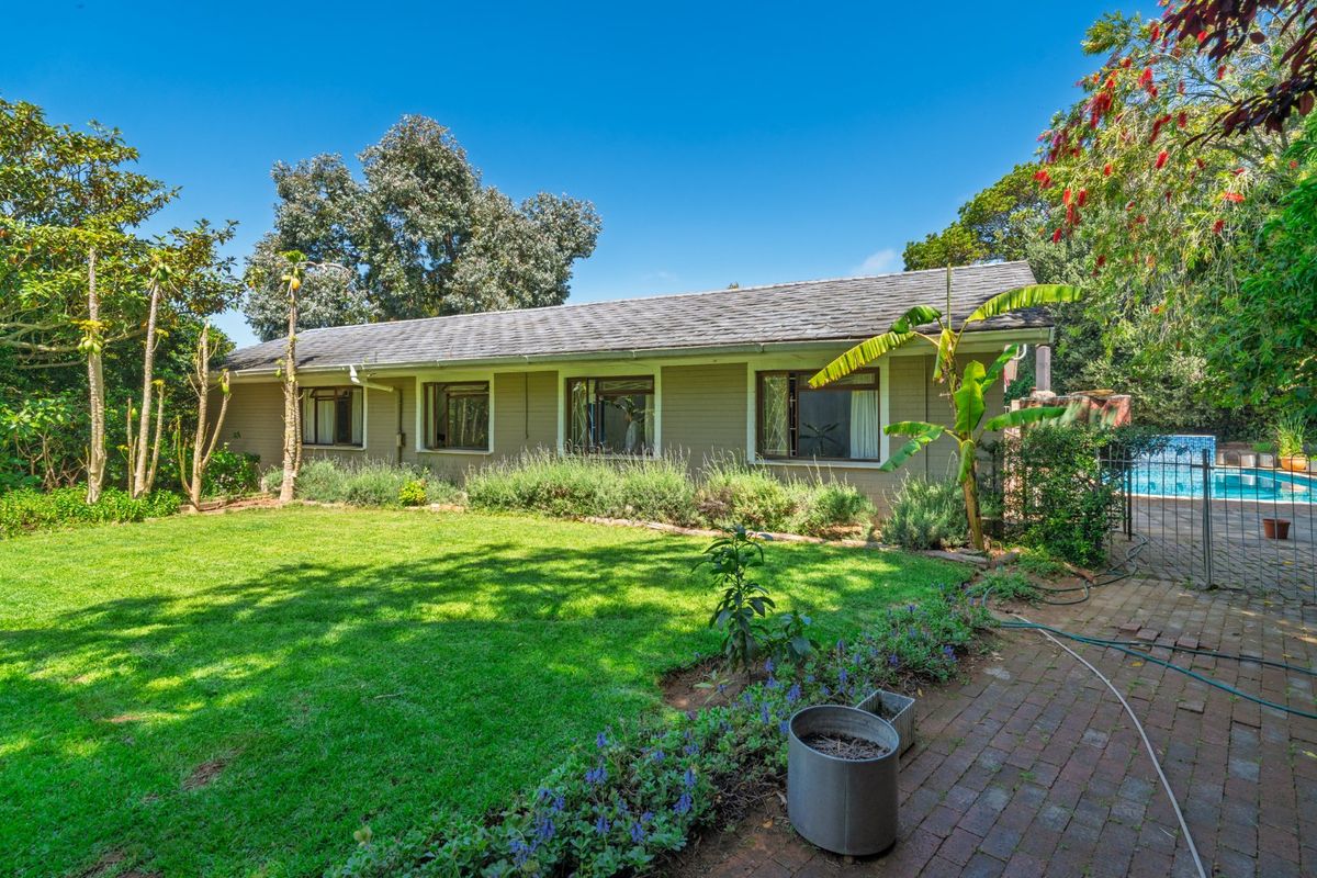Rear view of the house featuring a well-maintained lawn, landscaped garden beds, and a paved area leading to the swimming pool.