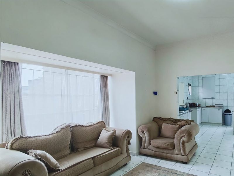 An open-plan living area featuring tiled flooring and a large bay window, with a view through to the adjacent kitchen space.