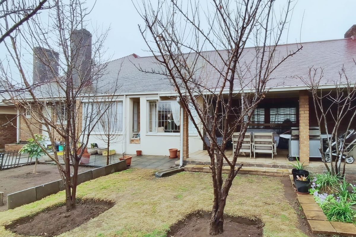 Rear view of the house featuring a covered patio area, brick chimneys, and a garden space with established trees.