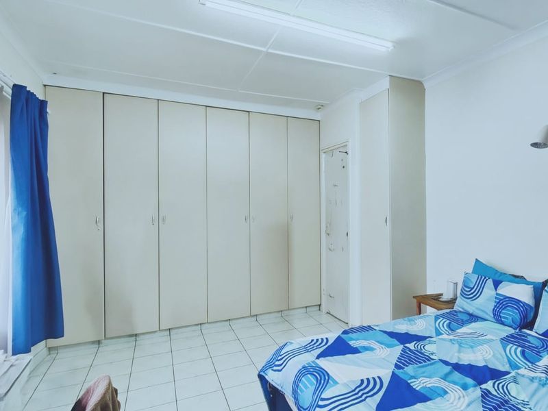 A bedroom featuring extensive built-in cupboards, tiled flooring, and a wall-mounted reading light.