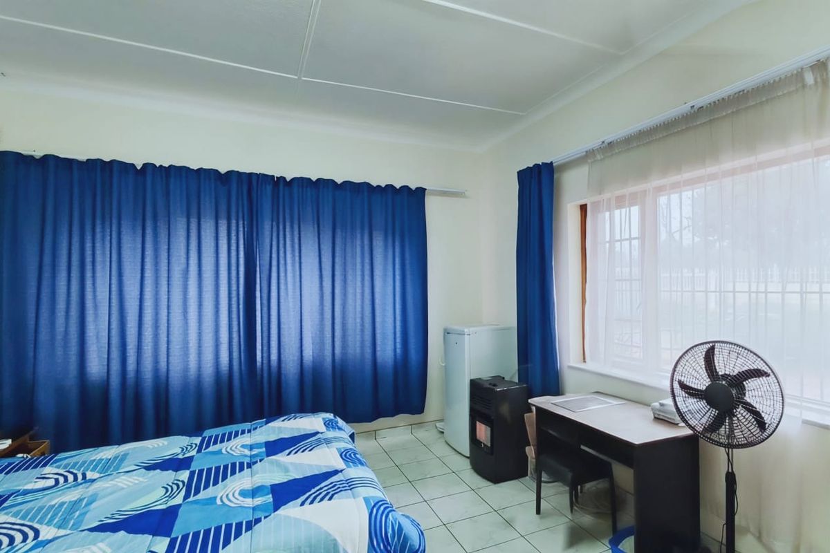 A bedroom featuring tiled flooring and large windows with curtain rails, providing a functional space with natural light.