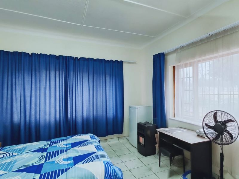 A bedroom featuring tiled flooring and large windows with curtain rails, providing a functional space with natural light.