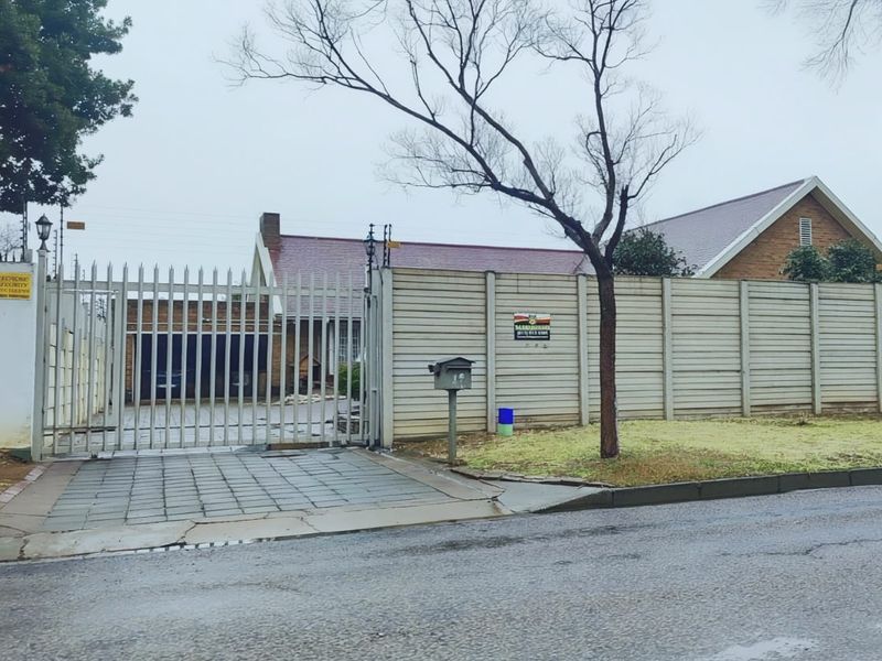 Front view of the property featuring a secure steel gate, paved driveway, and precast concrete boundary wall.