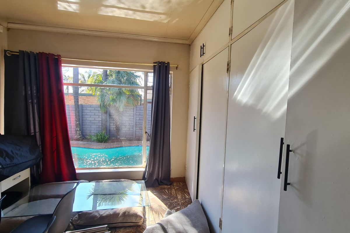 A bedroom featuring built-in cupboards and a large window with a view of the swimming pool area.