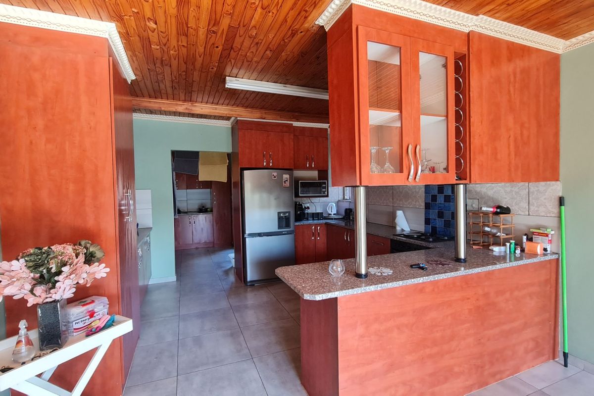 A functional kitchen featuring warm wooden ceilings, granite countertops, a breakfast bar, and ample built-in cabinetry, with an adjacent scullery area.