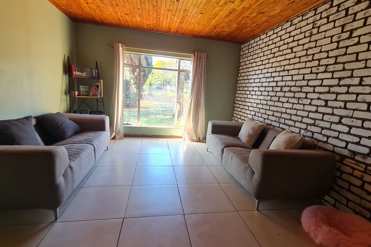 A living room featuring a rustic exposed brick wall, warm timber ceiling, and large window providing natural light and garden views.