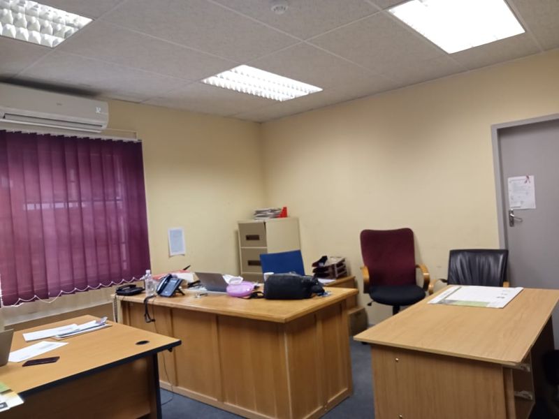 A functional commercial office space featuring a suspended ceiling with recessed lighting, wall-mounted air conditioning, and vertical window blinds.