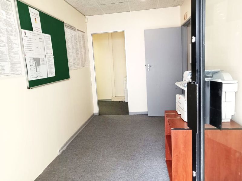 A functional commercial hallway featuring carpeted flooring, a suspended ceiling, and access to an adjoining office space.