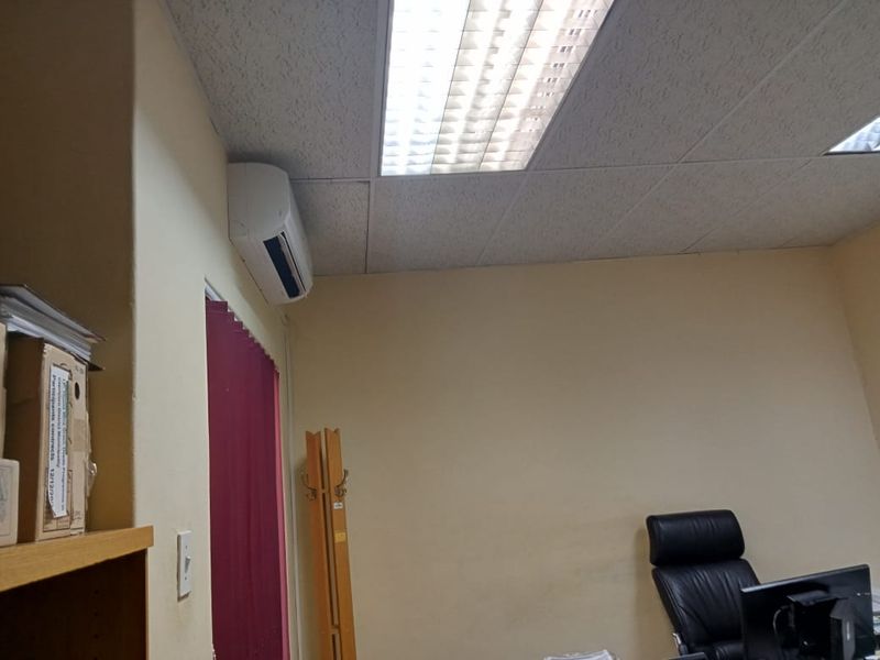 A functional office space featuring a suspended ceiling with recessed lighting and a wall-mounted air conditioning unit.