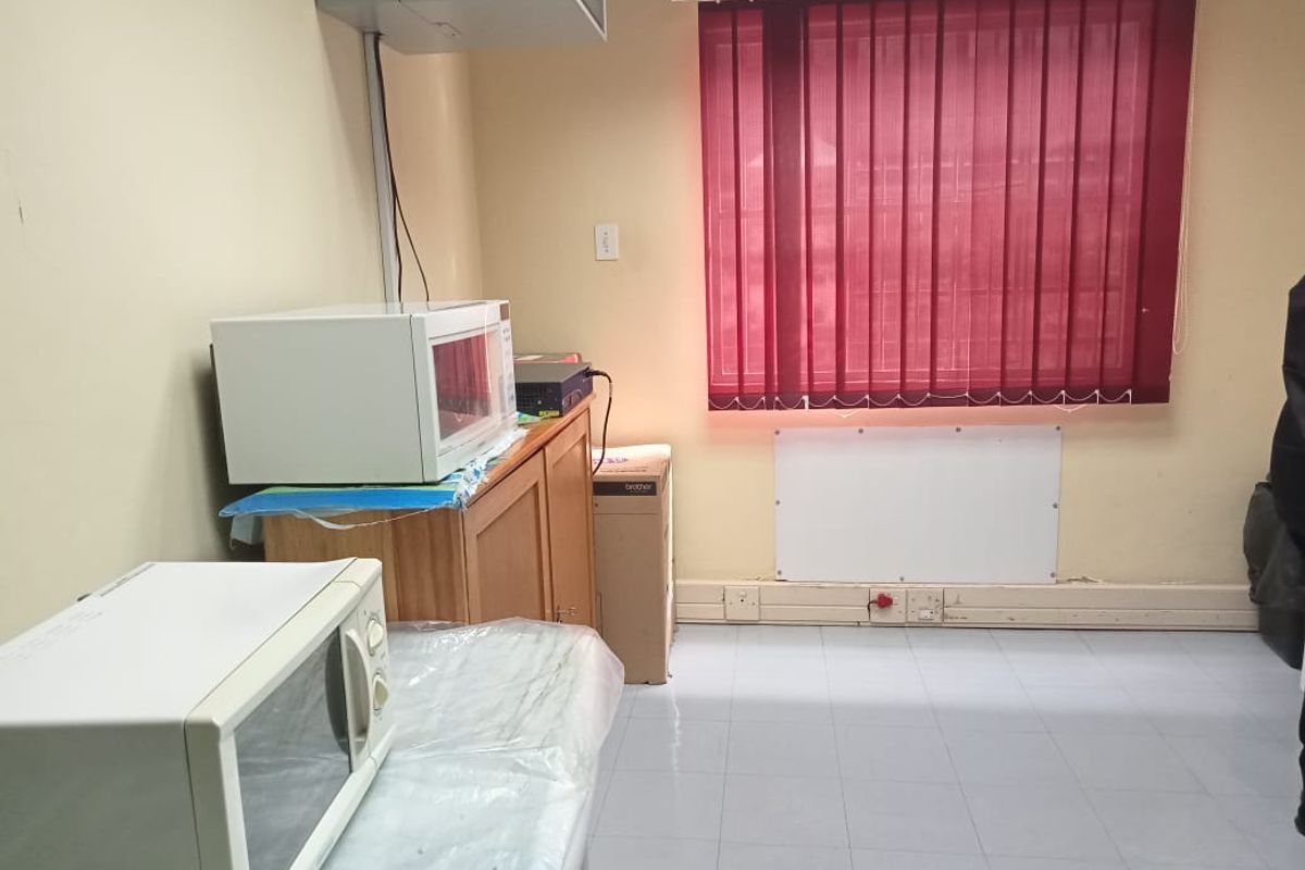 A functional commercial kitchen or breakroom area featuring tiled flooring, vertical window blinds, and wall-mounted electrical infrastructure.