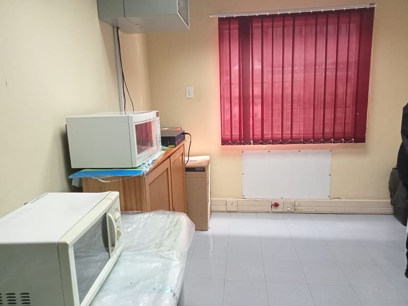 A functional commercial kitchen or breakroom area featuring tiled flooring, vertical window blinds, and wall-mounted electrical infrastructure.
