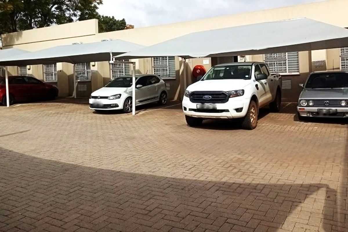 Commercial property exterior featuring a paved parking area with multiple shade cloth carports and security bars on the windows.