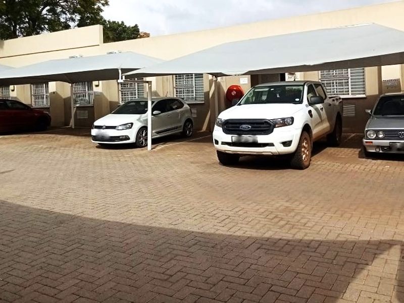 Commercial property exterior featuring a paved parking area with multiple shade cloth carports and security bars on the windows.