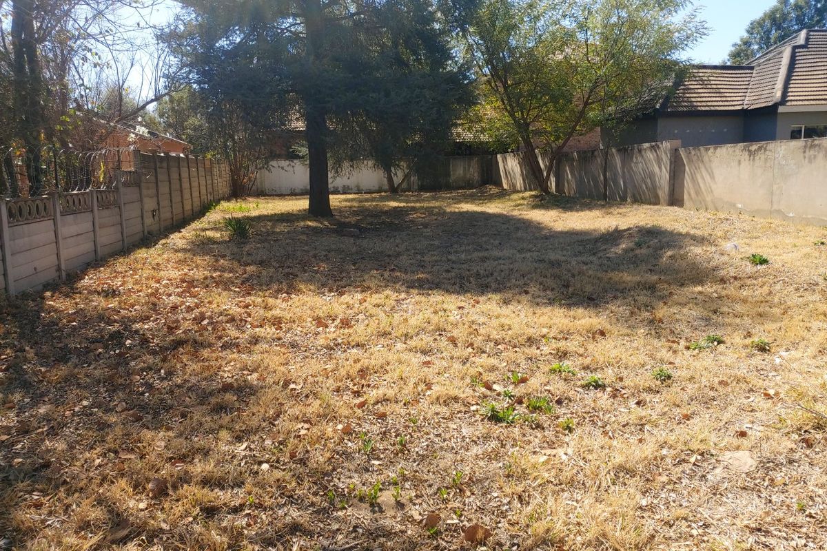 A vacant residential plot featuring established trees and perimeter boundary walls, offering a blank canvas for future development.