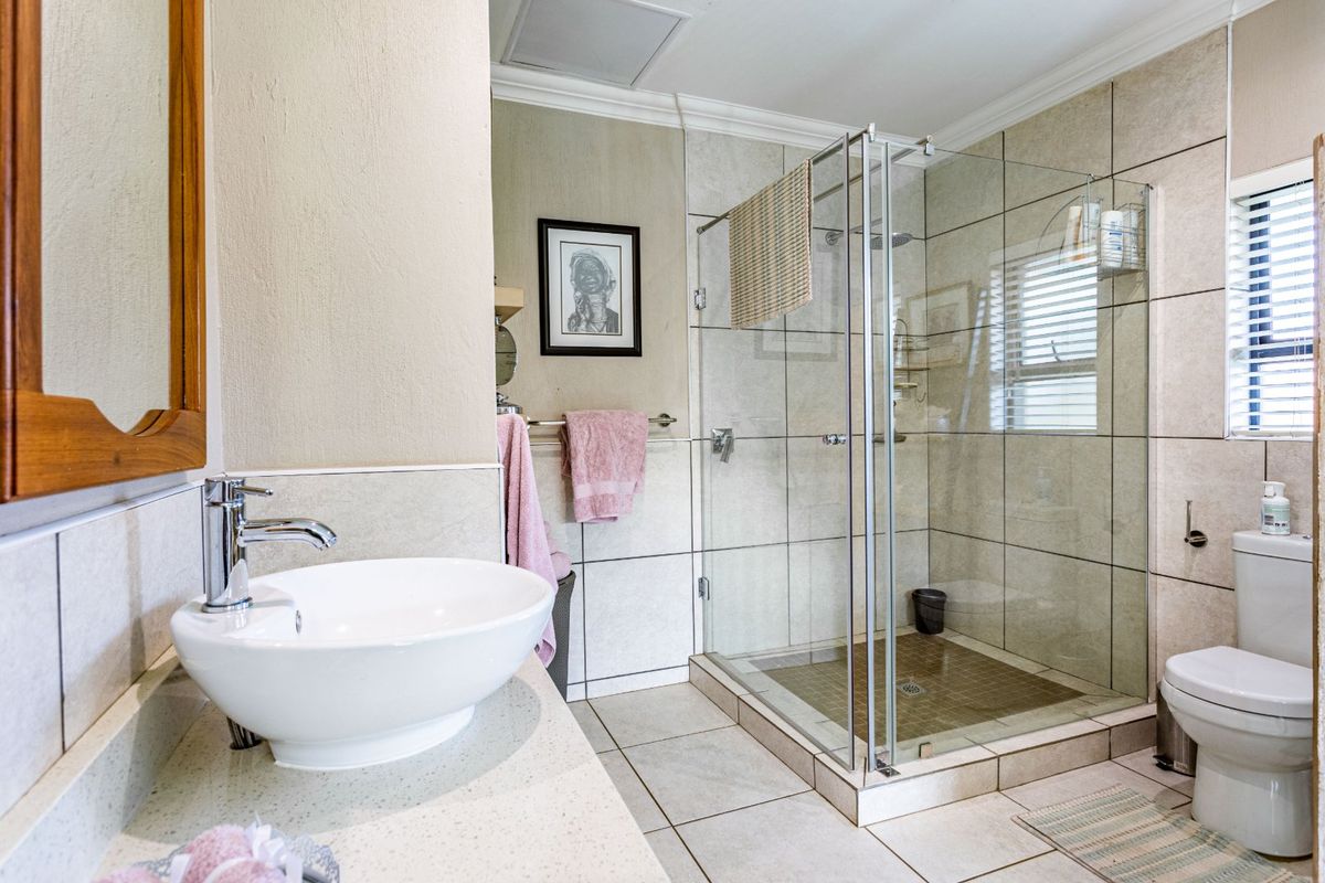 A well-maintained bathroom featuring a glass-enclosed shower, a modern vessel sink on a stone vanity, and neutral floor-to-ceiling tiling.