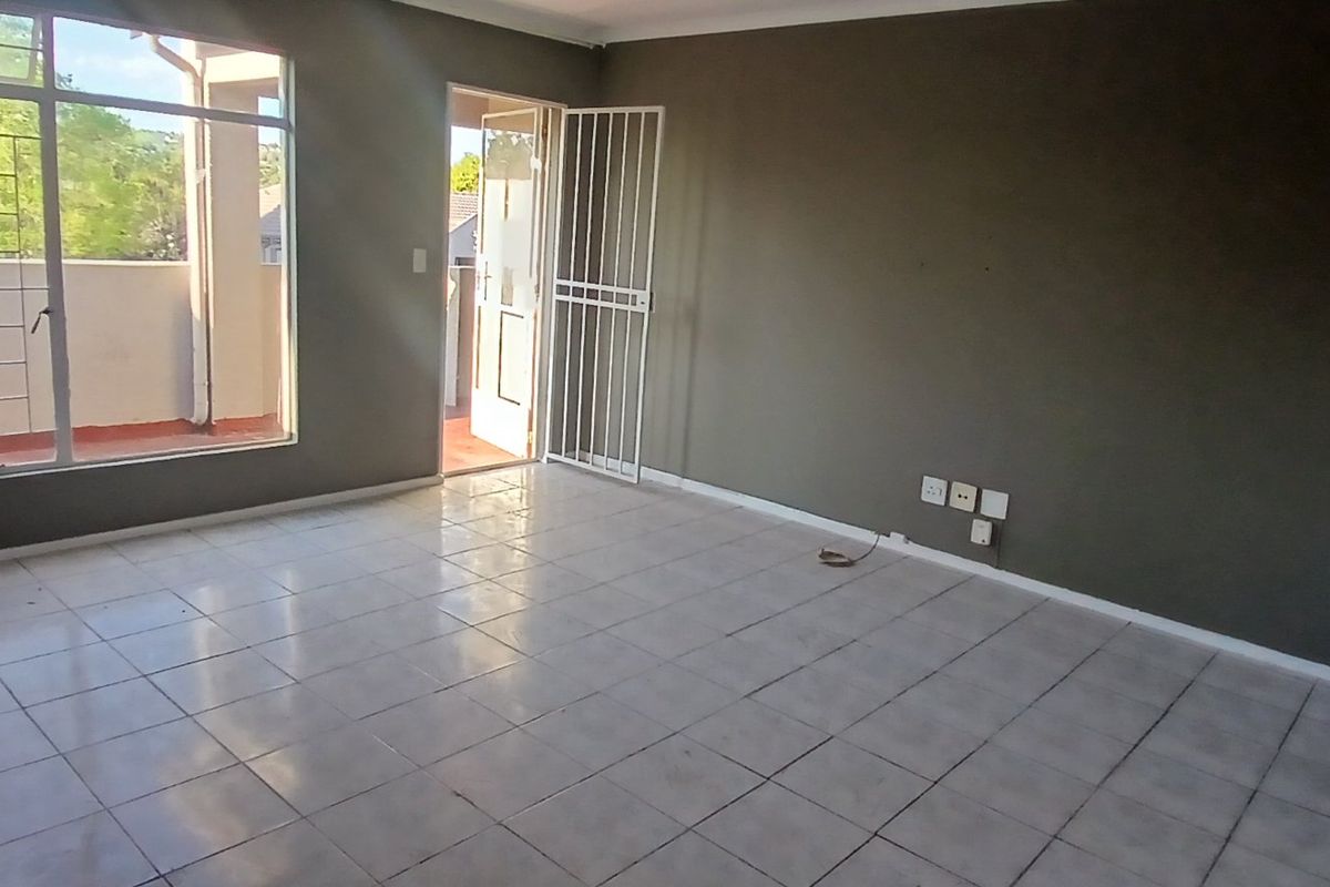 An empty living room featuring tiled flooring, a security gate, and access to an outdoor balcony area.