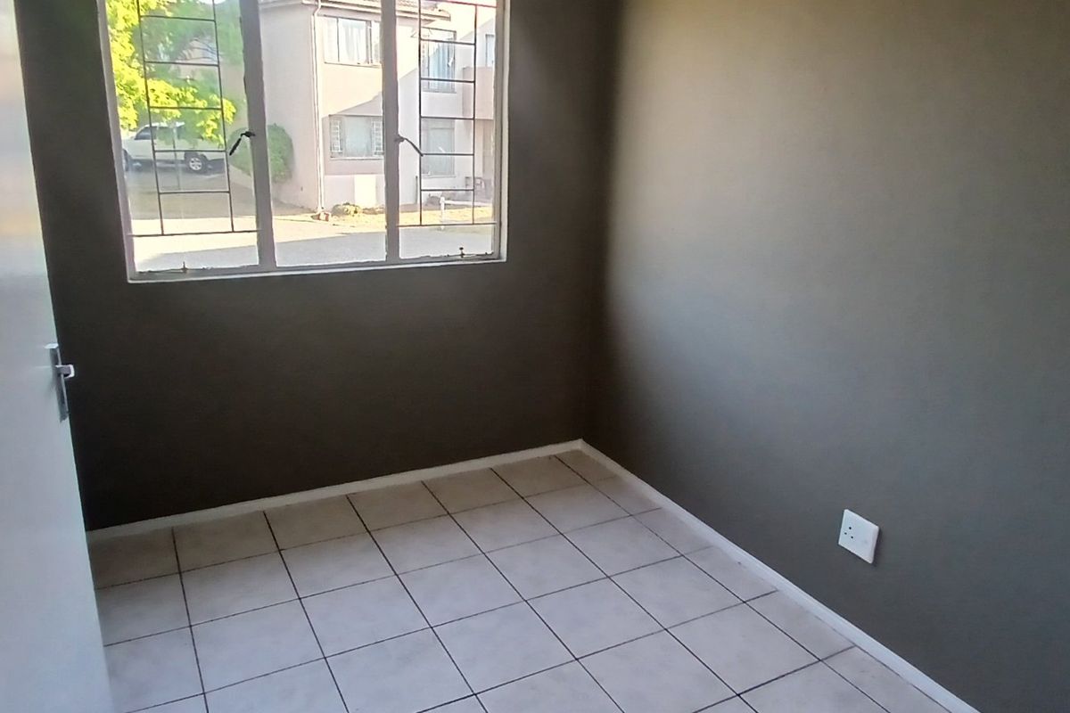 An empty bedroom featuring tiled flooring, dark grey walls, and a window fitted with security bars.