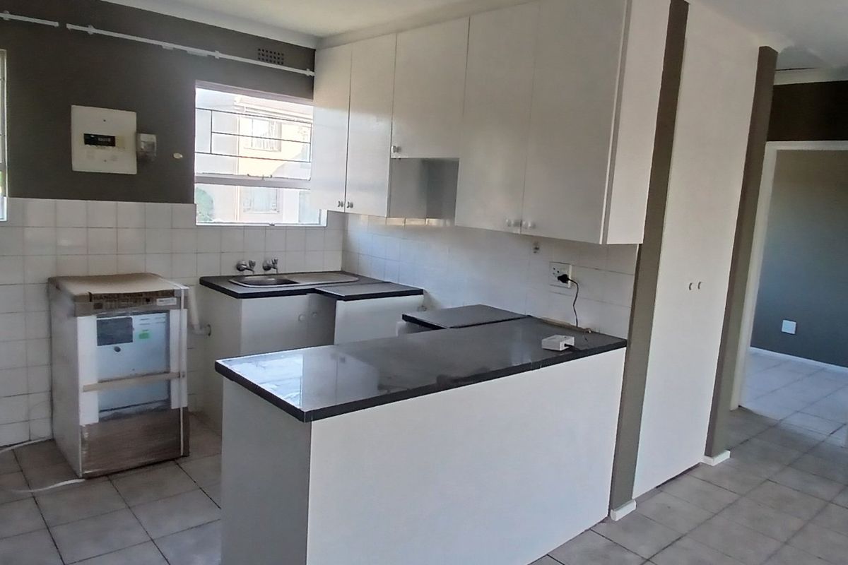 A functional kitchen featuring white cabinetry, dark countertops, tiled backsplash, and tiled flooring, offering a clean canvas for potential updates.