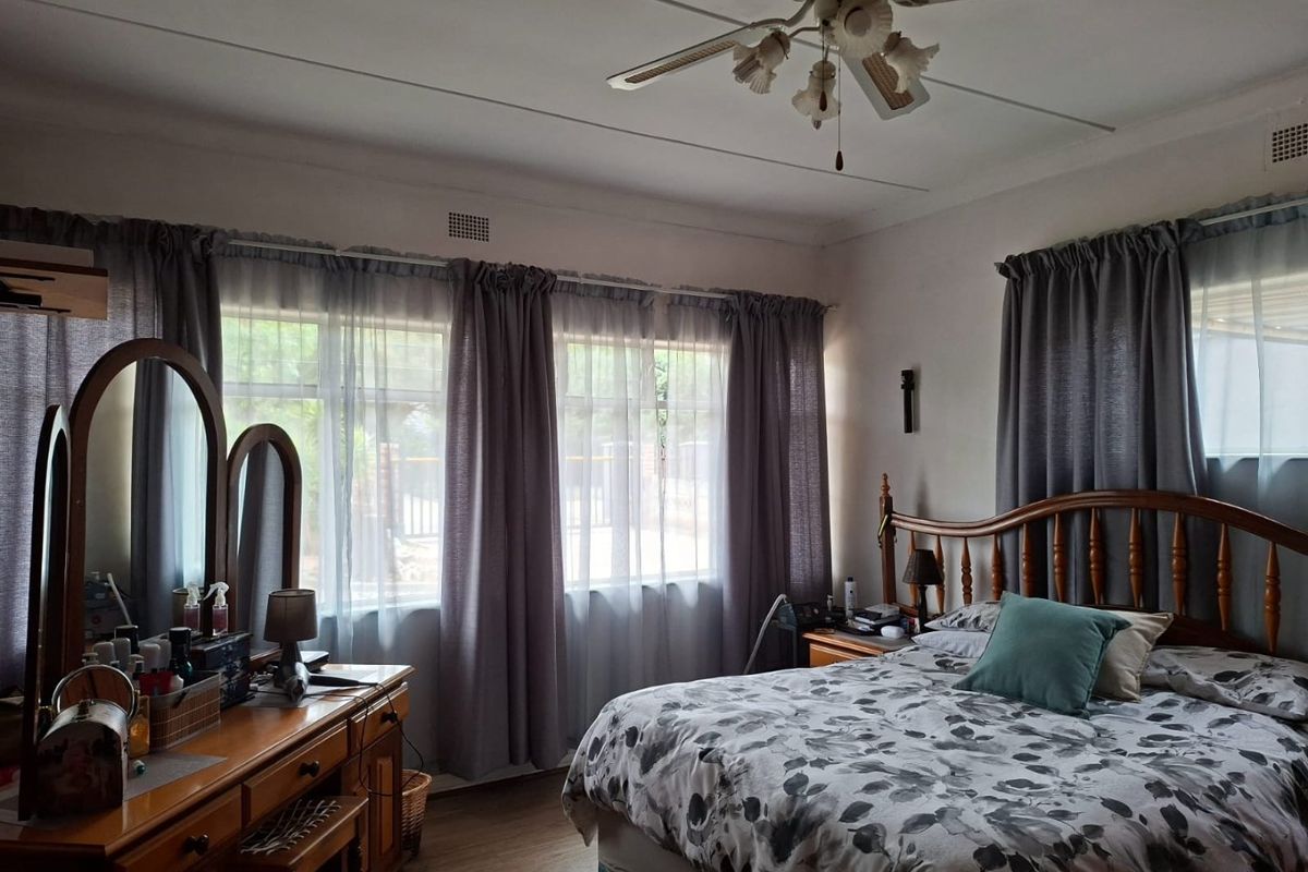 A well-lit bedroom featuring laminate flooring, a central ceiling fan, and large windows with curtain tracks.