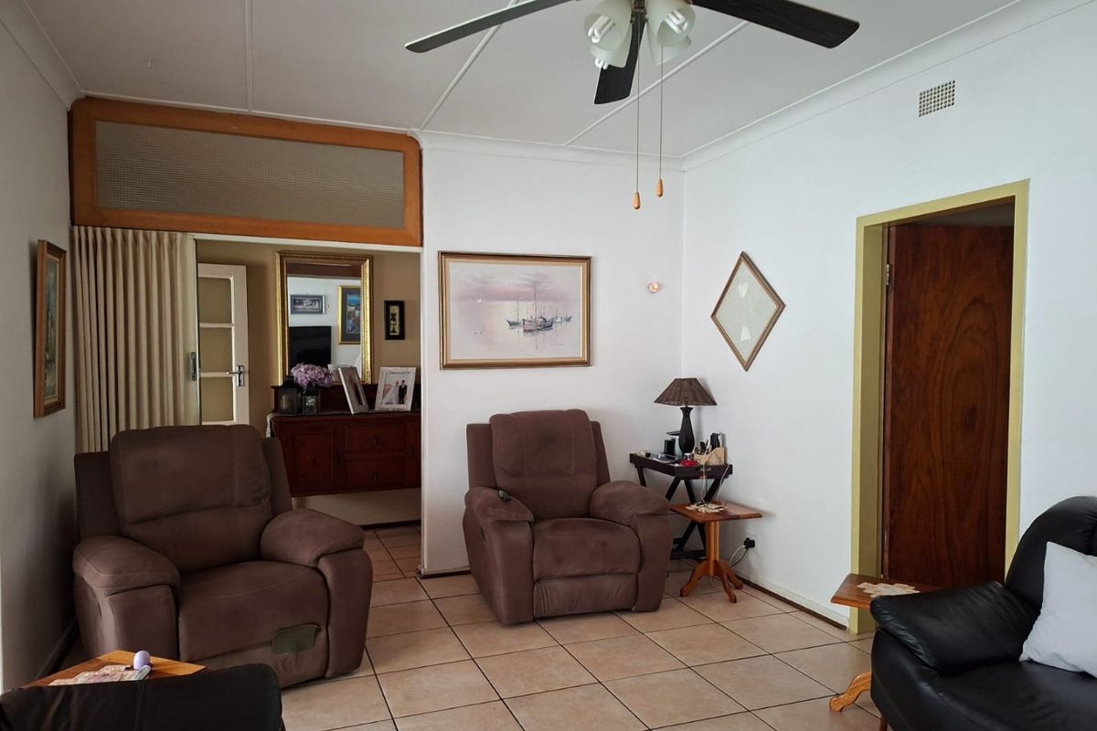 A living room featuring tiled flooring, a ceiling fan, and a wooden door frame, offering a functional and traditional layout.