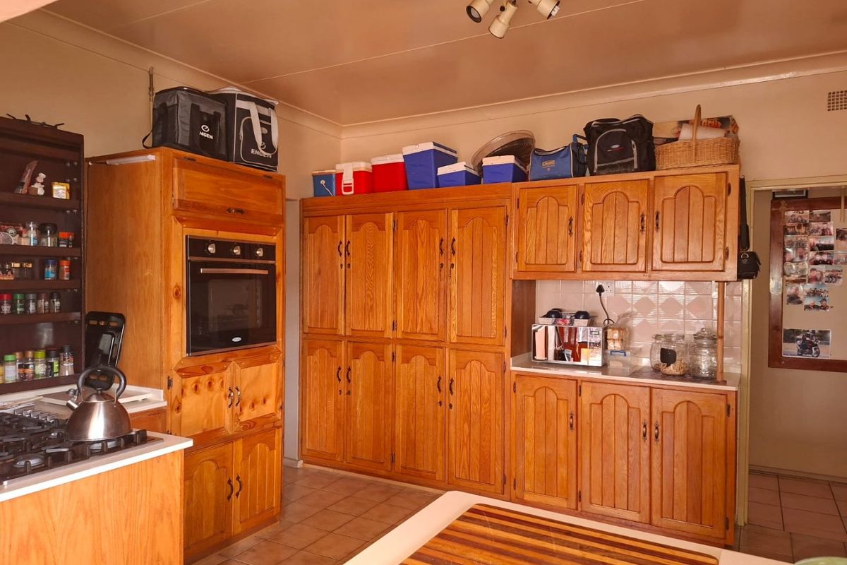 A functional kitchen featuring extensive wooden cabinetry, a built-in oven, gas hob, and tiled flooring, offering a traditional aesthetic with ample storage space.