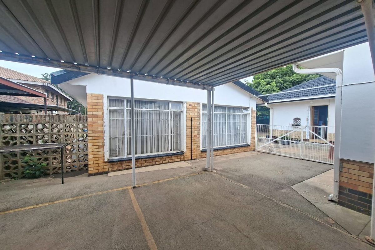 Rear exterior view featuring a covered carport, concrete driveway, and brick facade with large windows and a security gate.