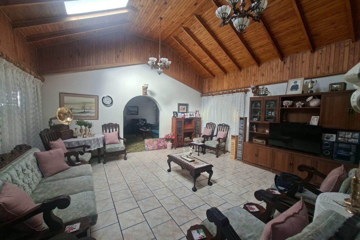 Spacious living room featuring a high vaulted timber ceiling with exposed beams, skylight, and tiled flooring, leading through an arched doorway to adjacent rooms.