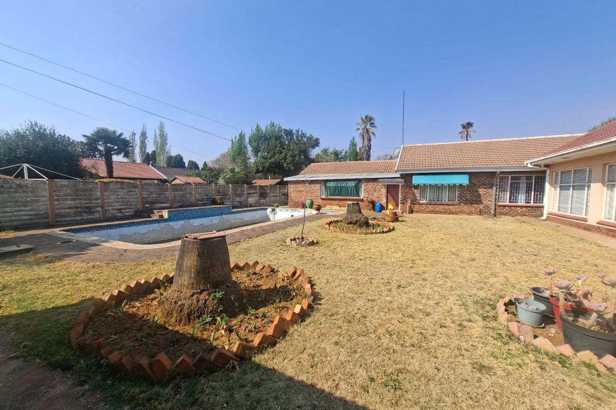Rear exterior view of the property featuring a large garden, an empty swimming pool, and brick facade with window awnings.