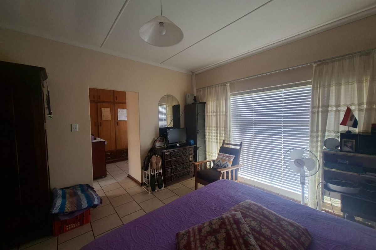 A bedroom featuring tiled flooring, a large window with blinds, and an adjoining walk-in closet area with built-in wooden cabinetry.