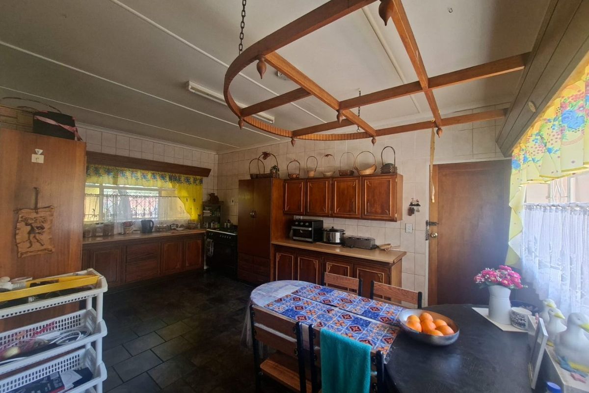 A spacious kitchen featuring traditional wooden cabinetry, tiled flooring, and a unique overhead timber feature, offering a functional layout with ample storage space.