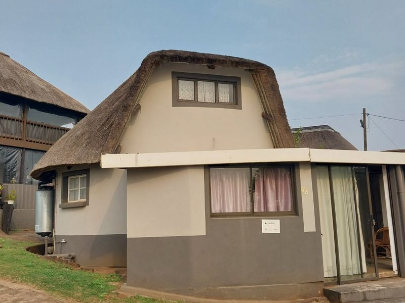 Front elevation of a townhouse featuring a distinctive thatch roof, aluminium window frames, and a sliding glass door entrance.