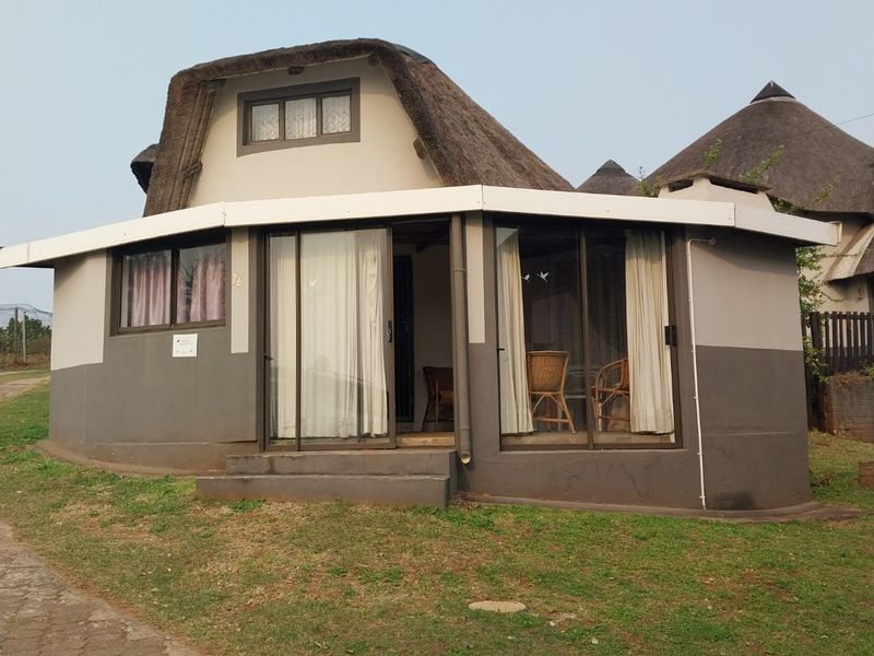 Front elevation of a townhouse featuring a distinctive thatched roof, sliding glass doors, and a small concrete entrance step.