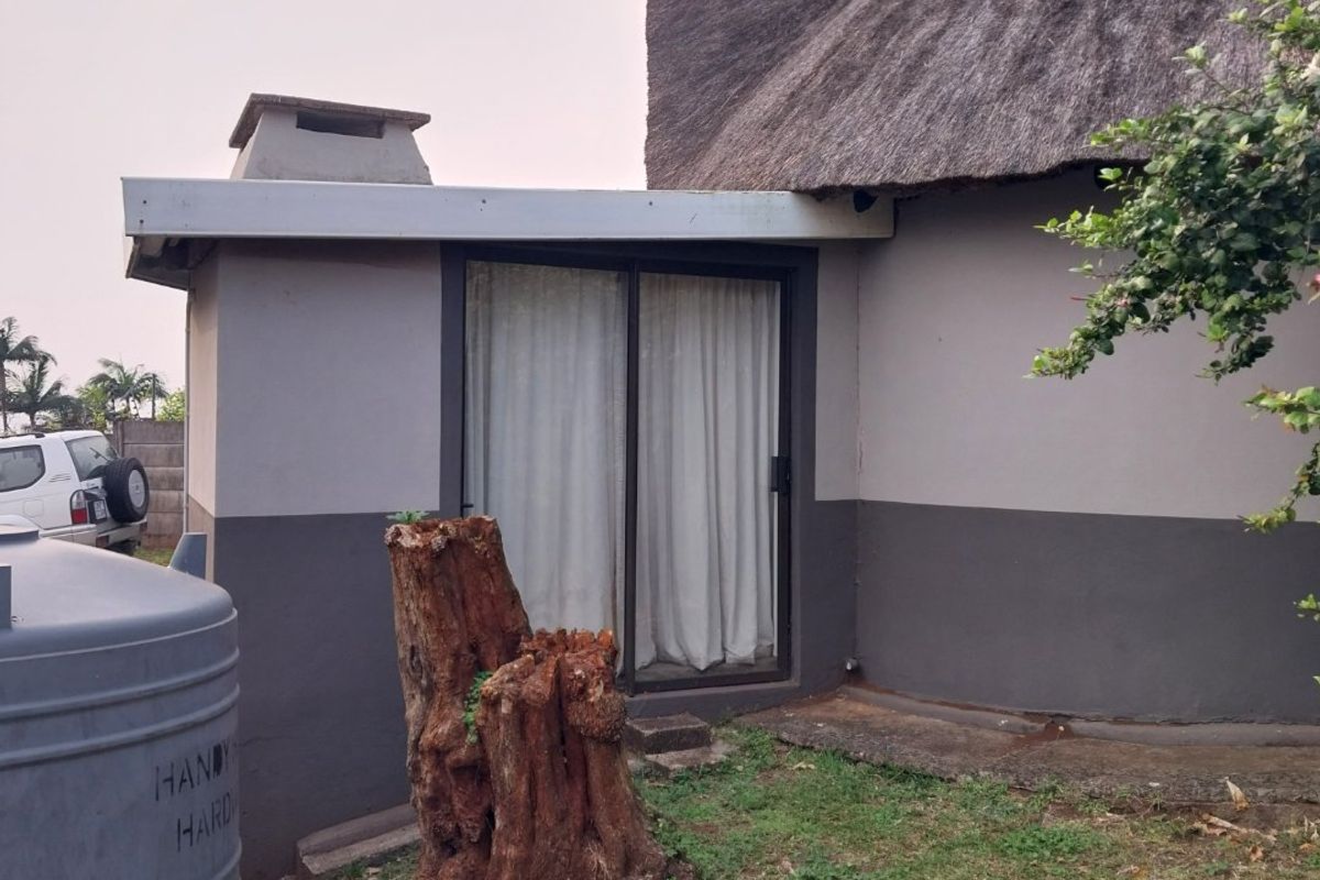 Rear exterior view of a townhouse featuring a thatched roof, sliding glass door access, and a water tank situated in the garden area.