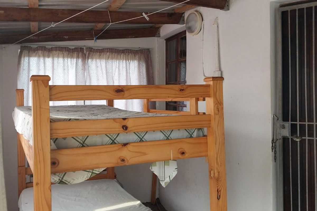 A bedroom featuring exposed timber rafters and corrugated roofing, with a security gate entrance and basic wall finishes.