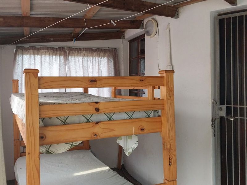 A bedroom featuring exposed timber rafters and corrugated roofing, with a security gate entrance and basic wall finishes.