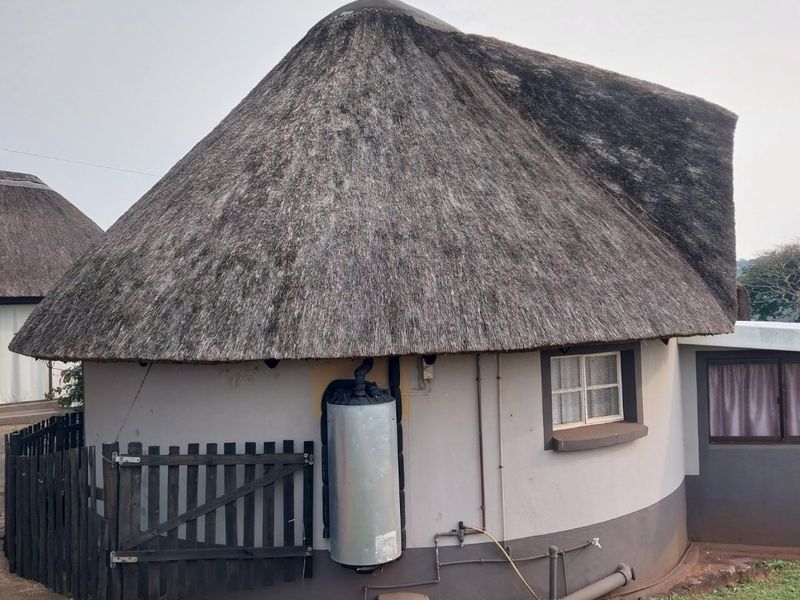 Rear view of a circular townhouse unit featuring a traditional thatch roof, external geyser, and timber picket fencing.