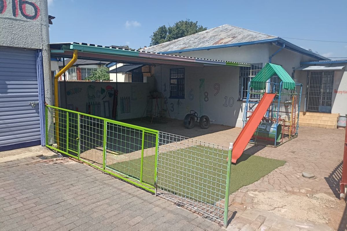 Rear exterior area featuring a paved courtyard, perimeter wall, and corrugated metal roof structure, currently utilized as an outdoor play space.