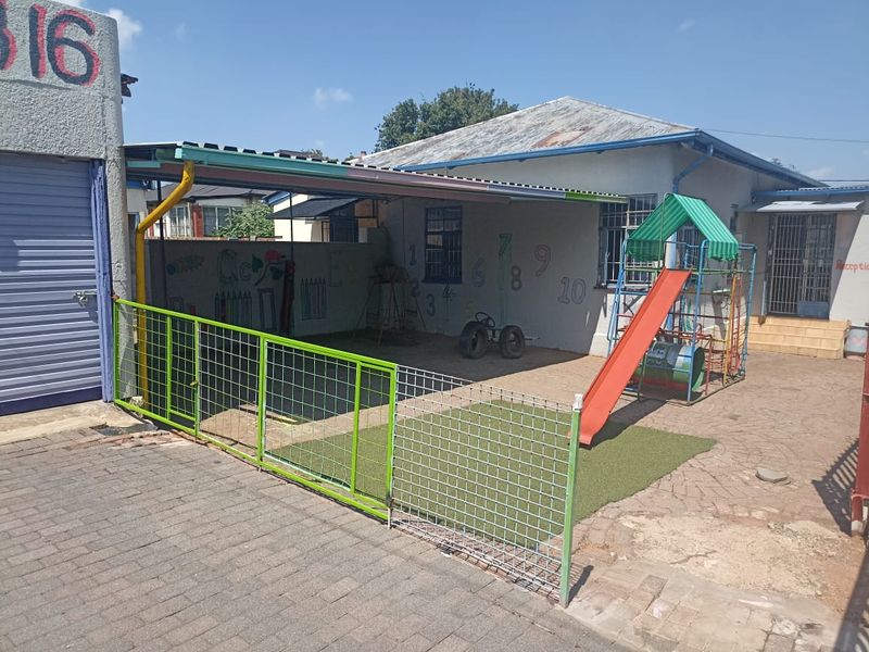 Rear exterior area featuring a paved courtyard, perimeter wall, and corrugated metal roof structure, currently utilized as an outdoor play space.
